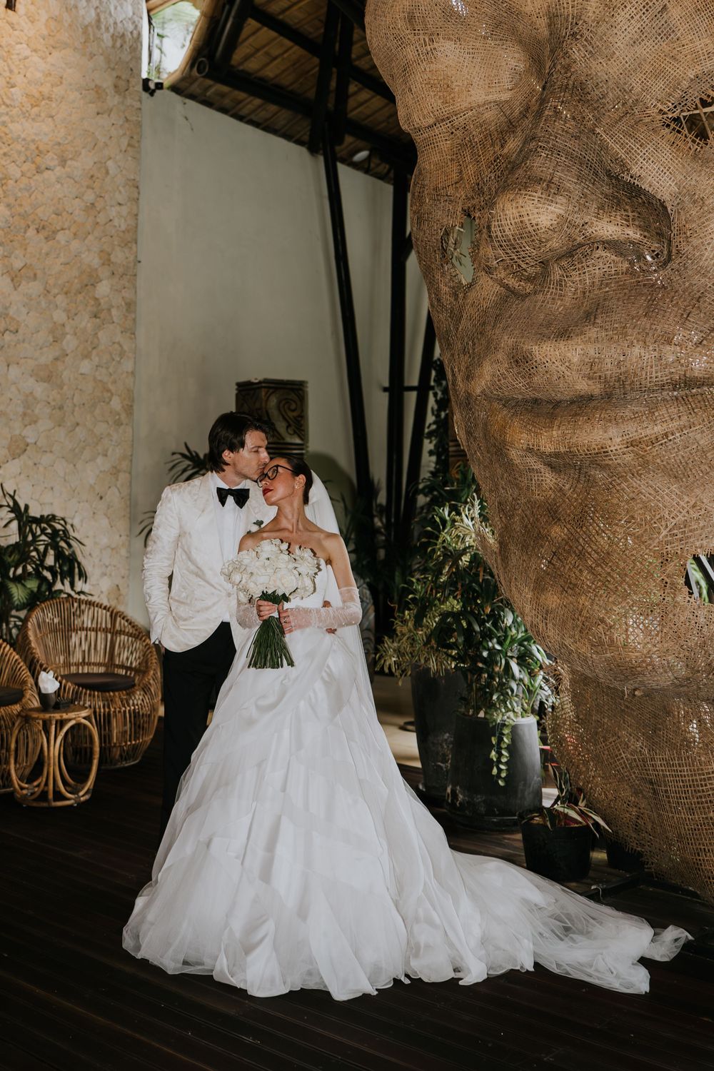 Romantic wedding couple poses on vintage furniture against a textured wall backdrop.