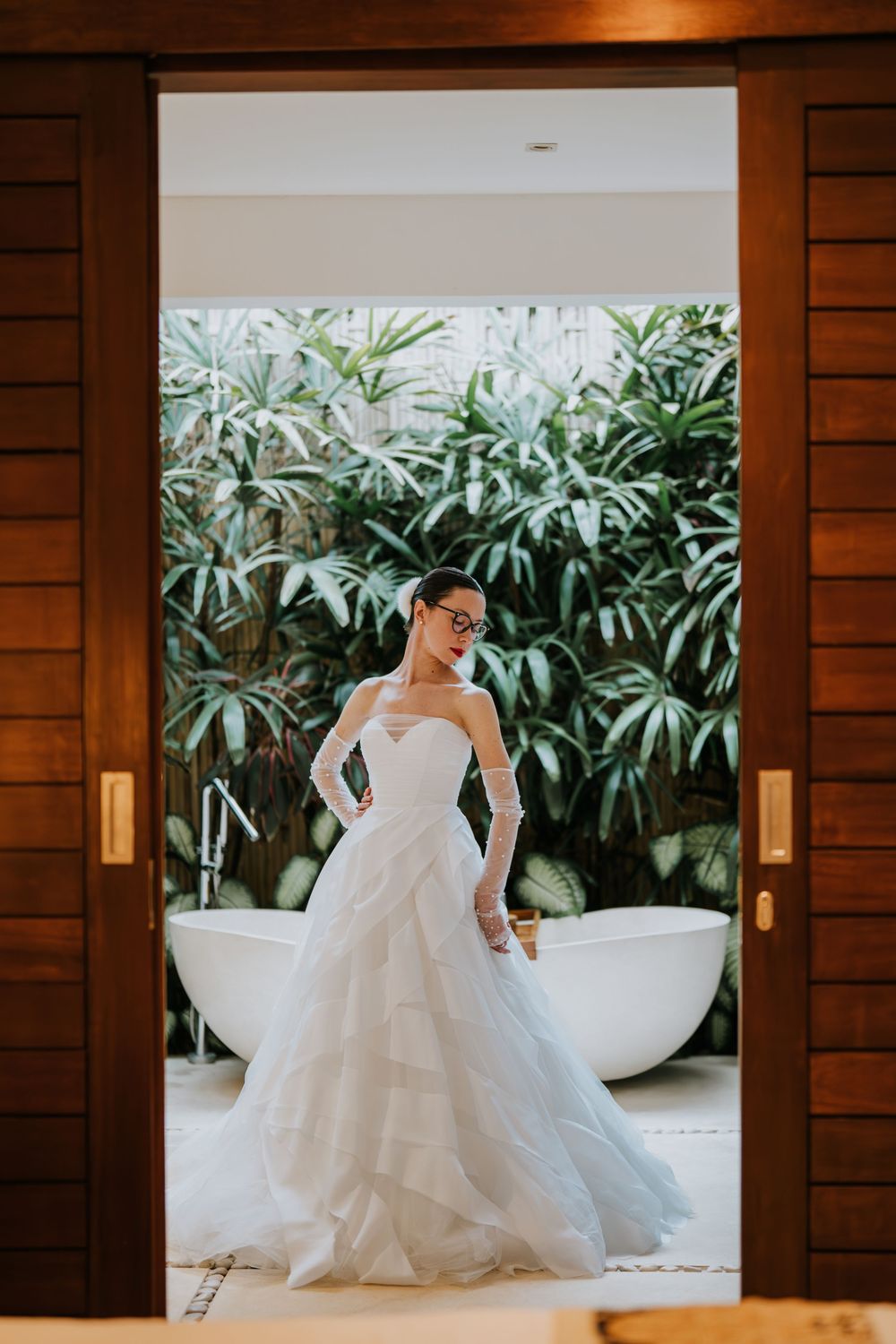 A series of elegant photos showing a bride in a white gown posing near a modern bathtub with tropical plants in background.