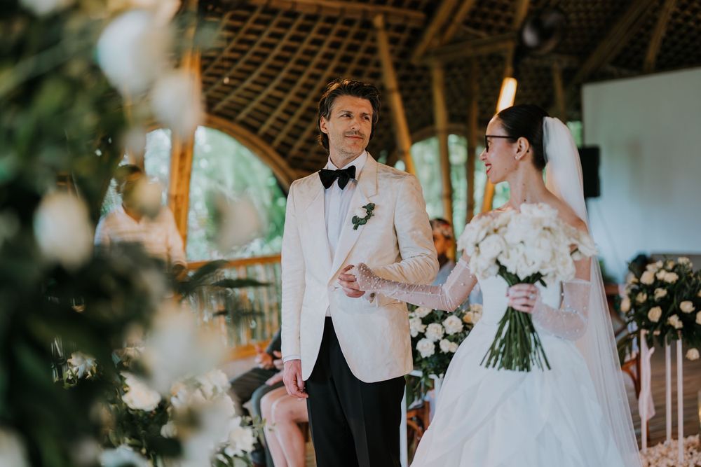 Outdoor wedding ceremony scene with floral decorations and gathered guests.
