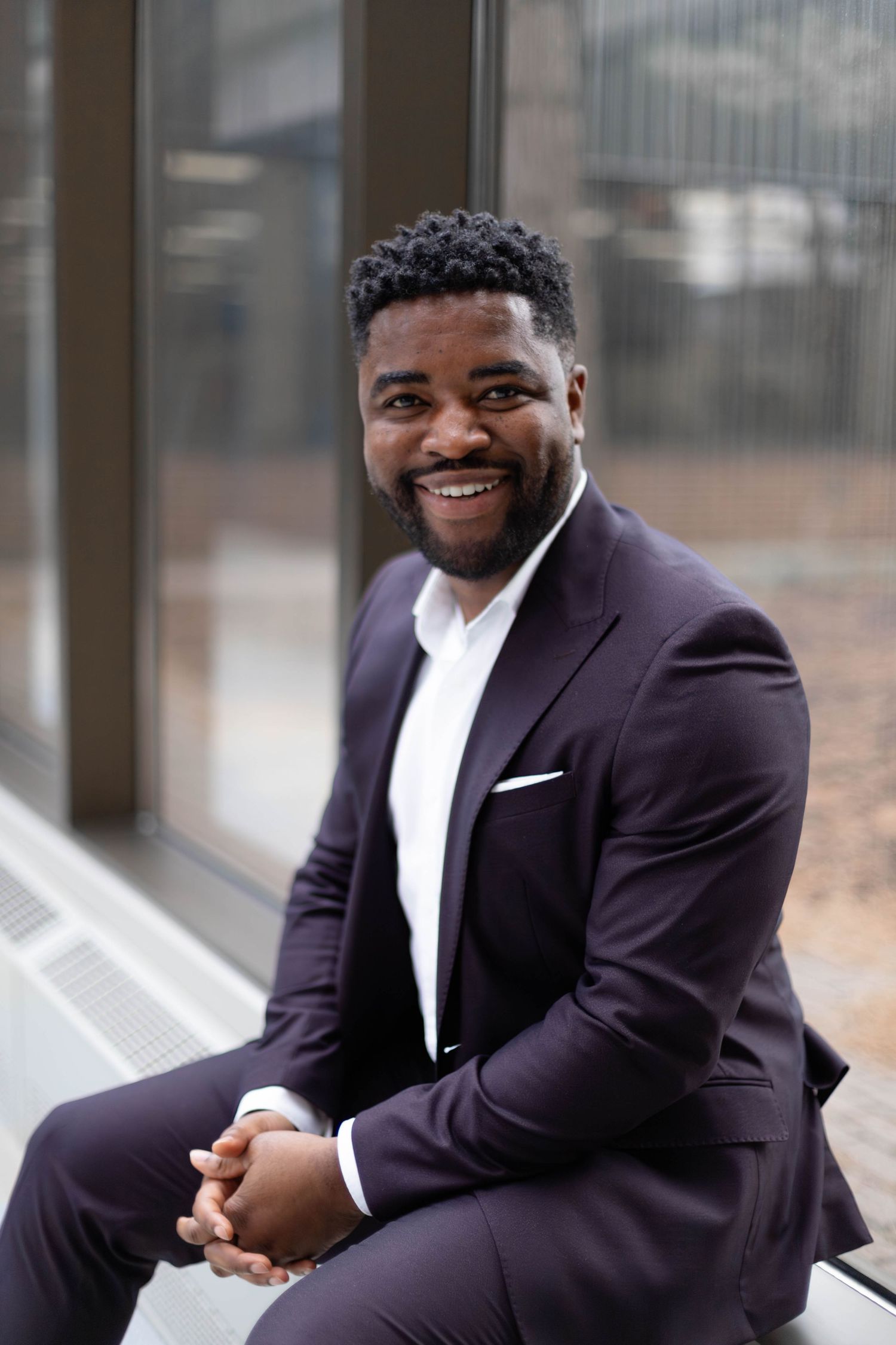 A collage of four professional portraits showing someone in a black suit and white shirt smiling in different poses.