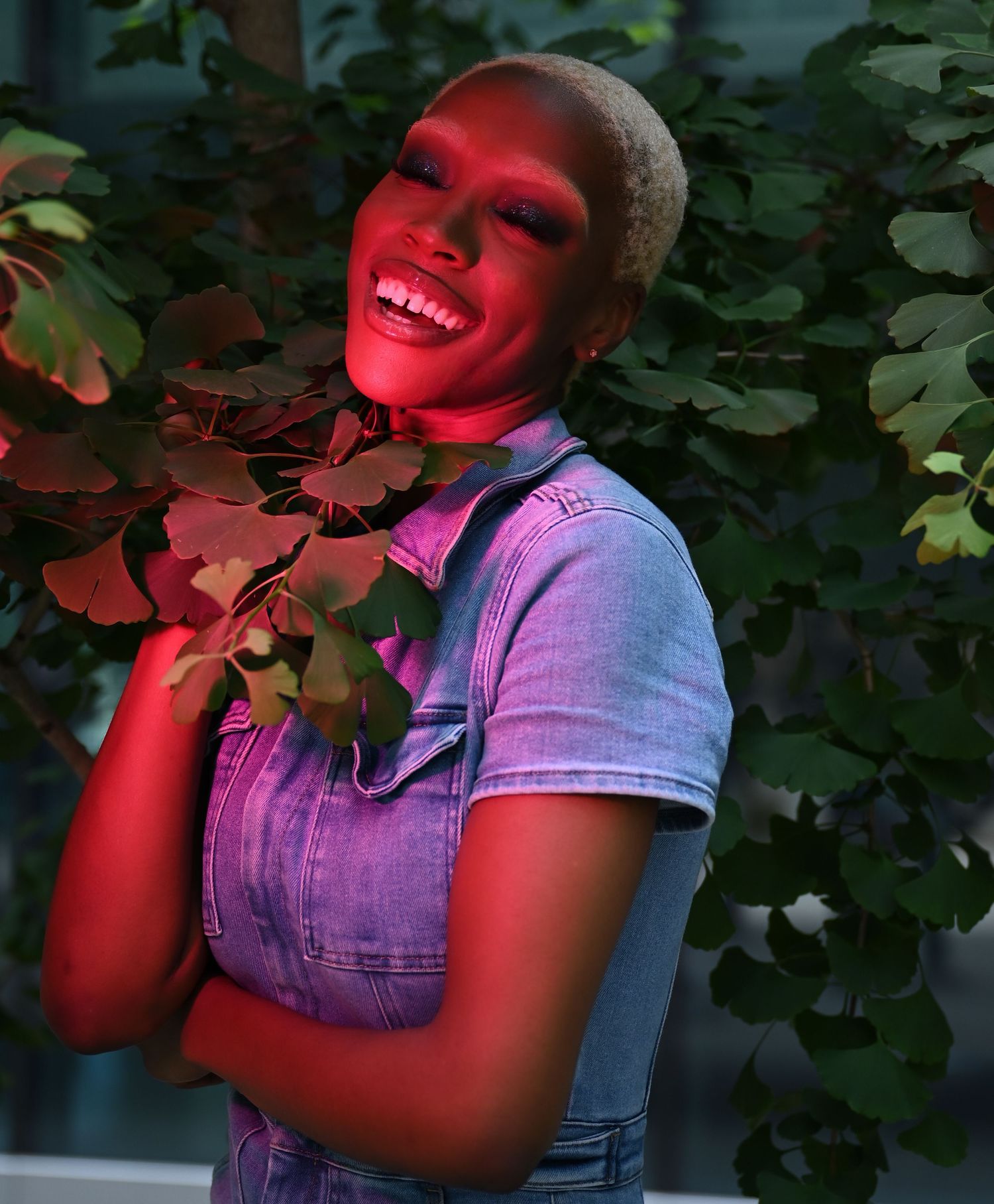 Person wearing light blue denim overalls strikes playful poses against brick wall in four panel sequence.