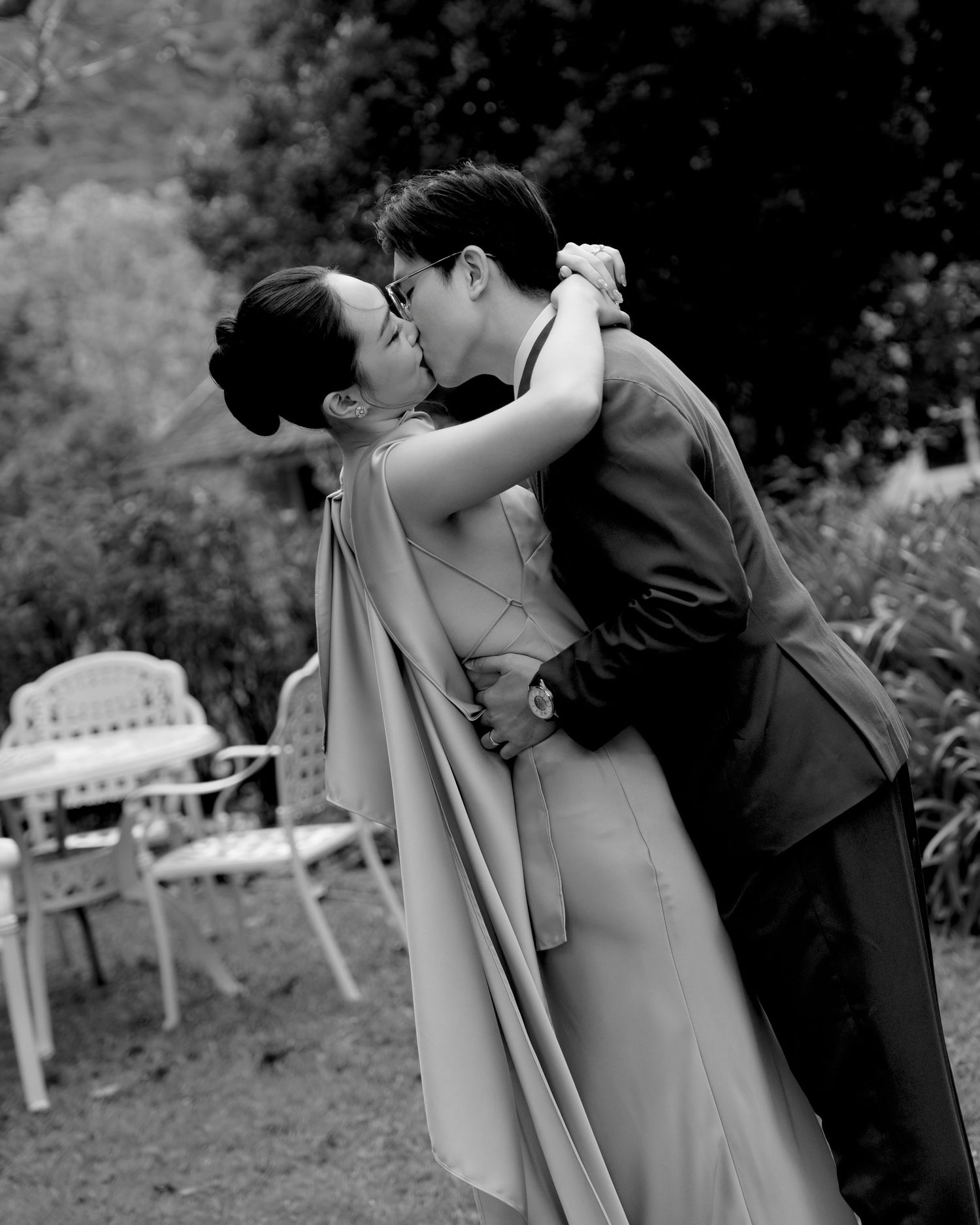 Couple sharing a romantic kiss outdoors in a lush garden in black and white.