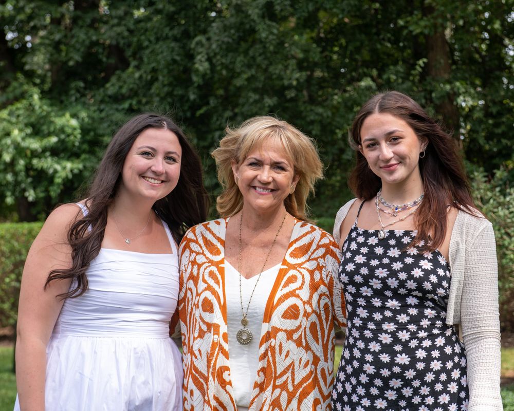 Three generations pose together outdoors wearing summer dresses and bright patterns.
