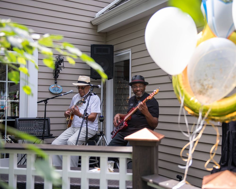 Musicians performing on porch with balloons and festive decorations.