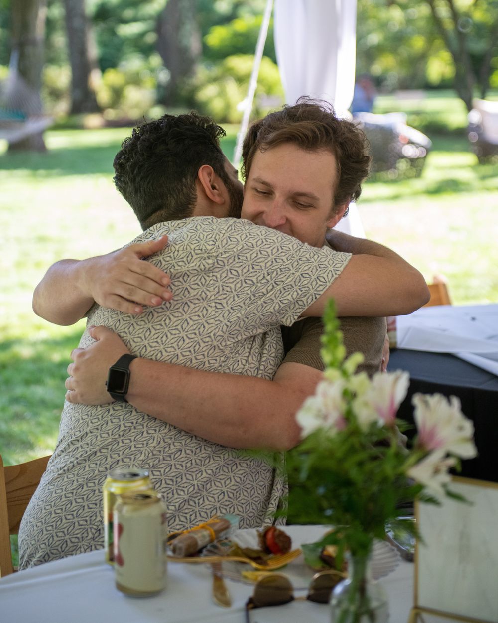 Two people sharing an emotional embrace at an outdoor dining table.