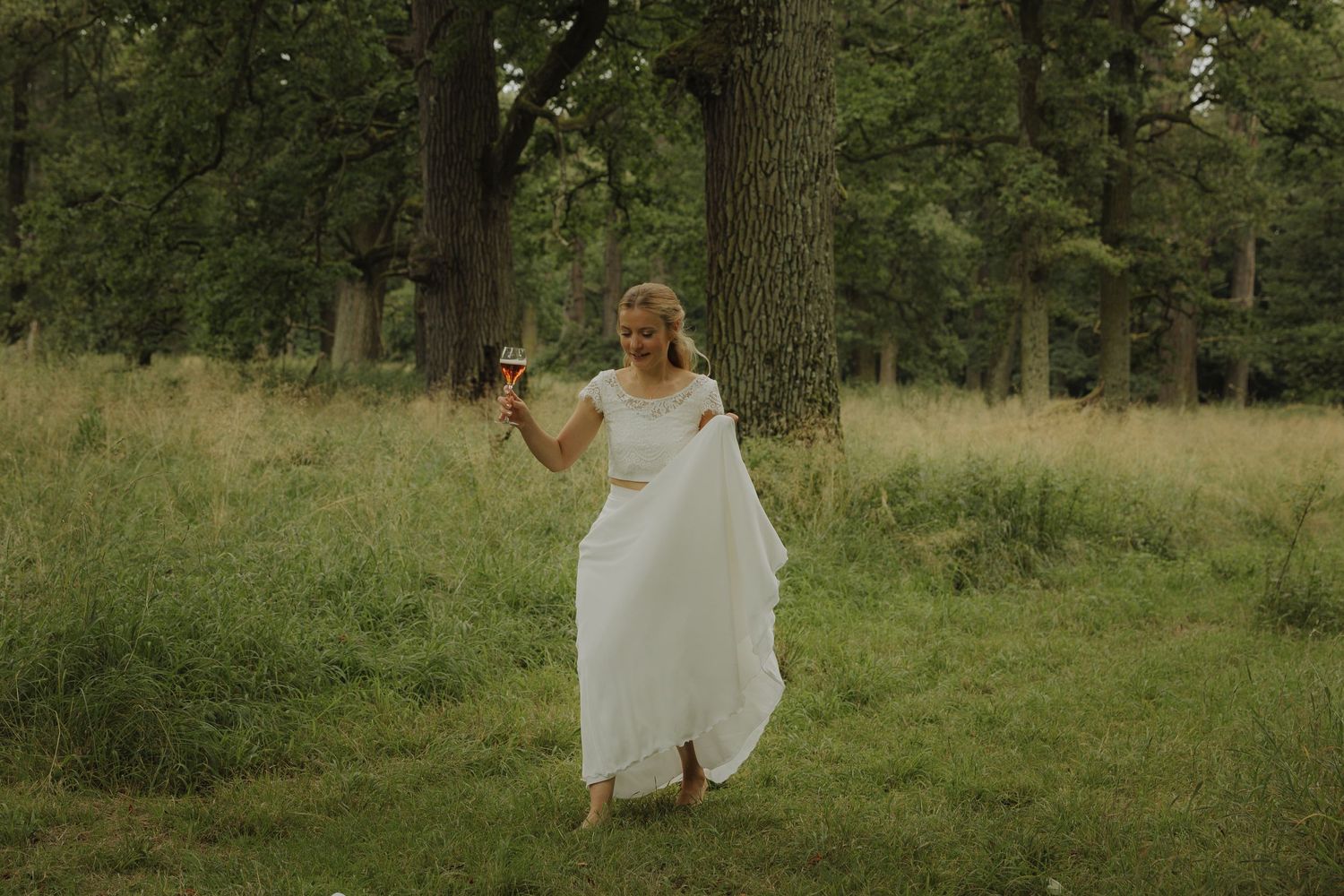 A couple strolls through a green forest clearing during their outdoor celebration.