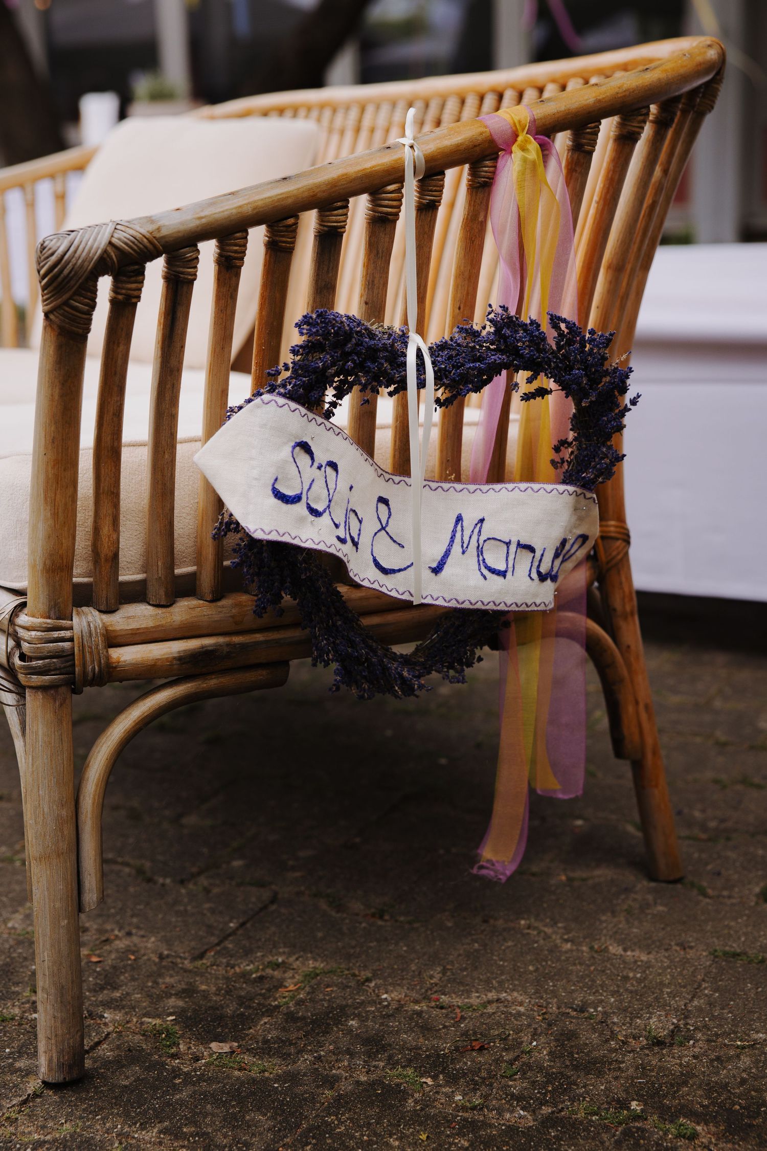 Bamboo chair decorated with purple flowers and a handwritten sign at a wedding.