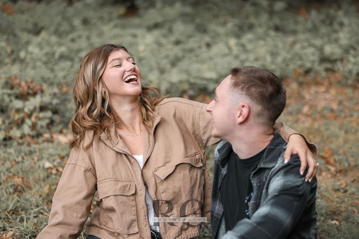 A couple shares a joyful moment of laughter together outdoors wearing casual fall attire.