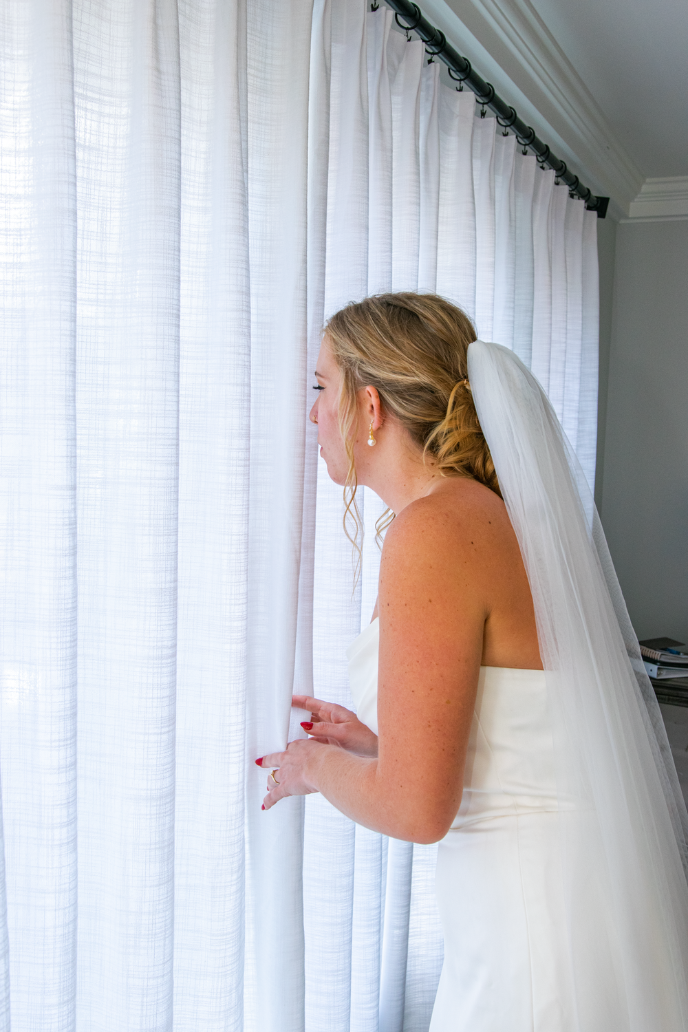 Bride in white dress peeks through sheer curtains in sequence of photos.