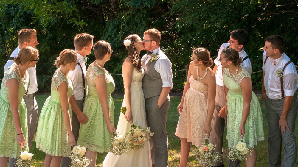 Wedding party in mint green and blush dresses poses outdoors in a garden setting.