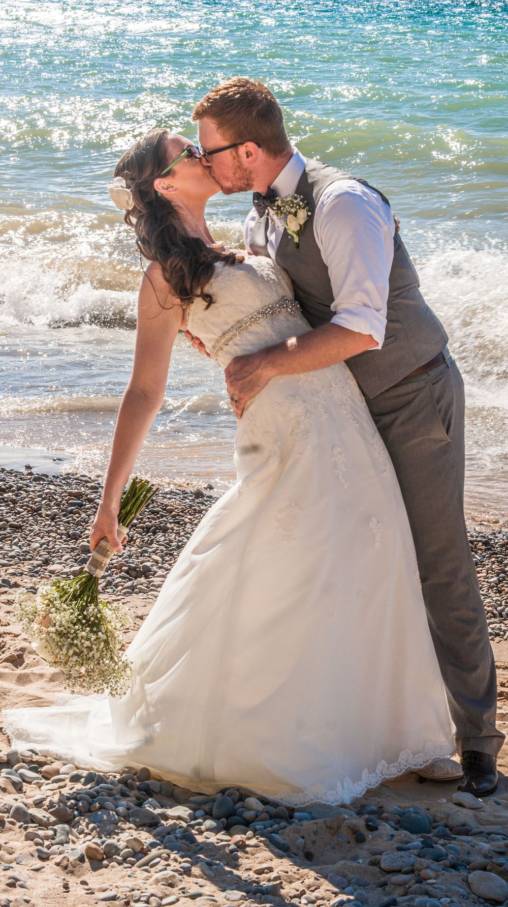 Romantic beach wedding photos with couple posing by ocean waves on rocky shore.