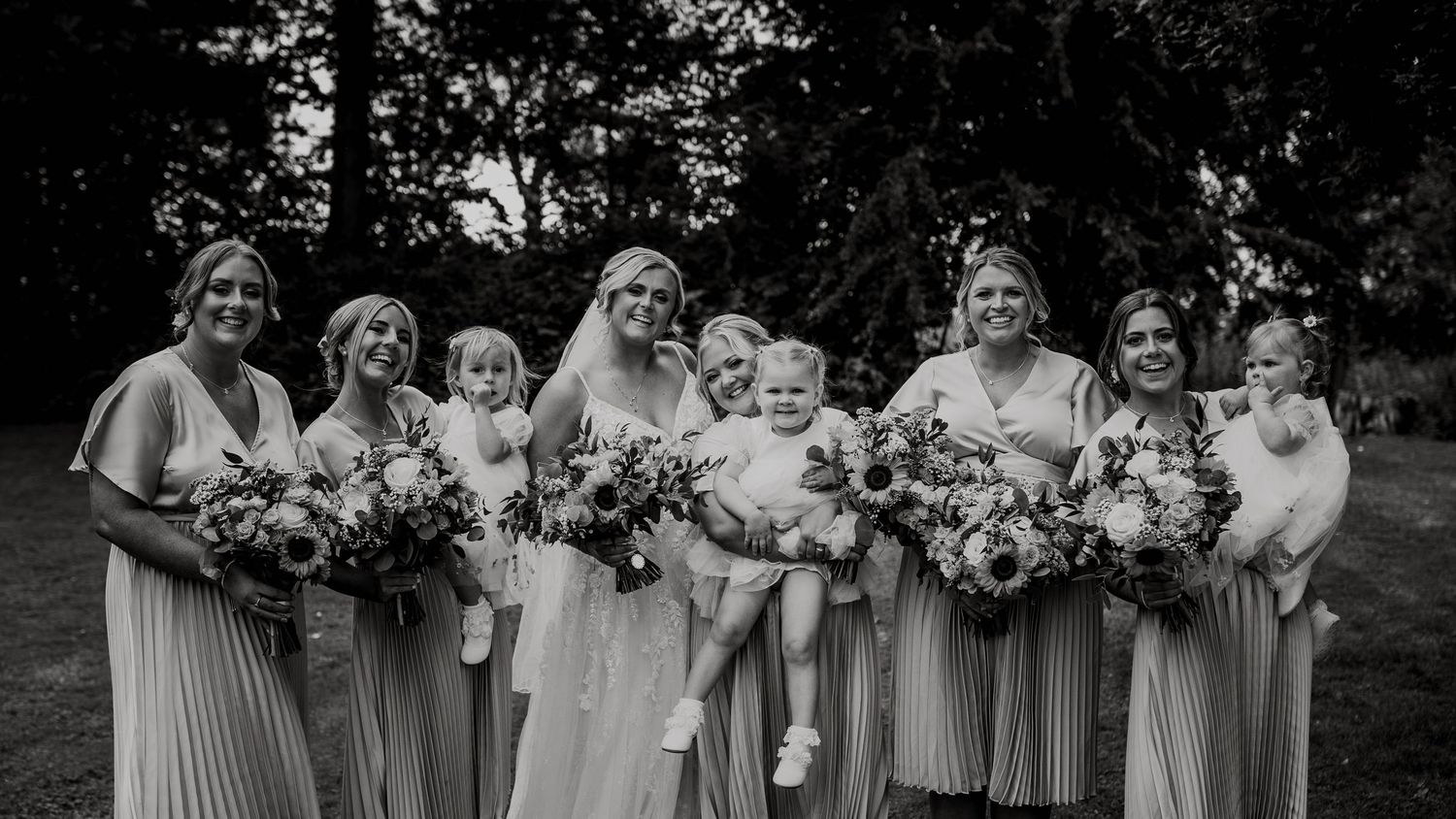 Black and white group photo of bridesmaids holding bouquets in flowing dresses. Houchins wedding venue. Essex photographers