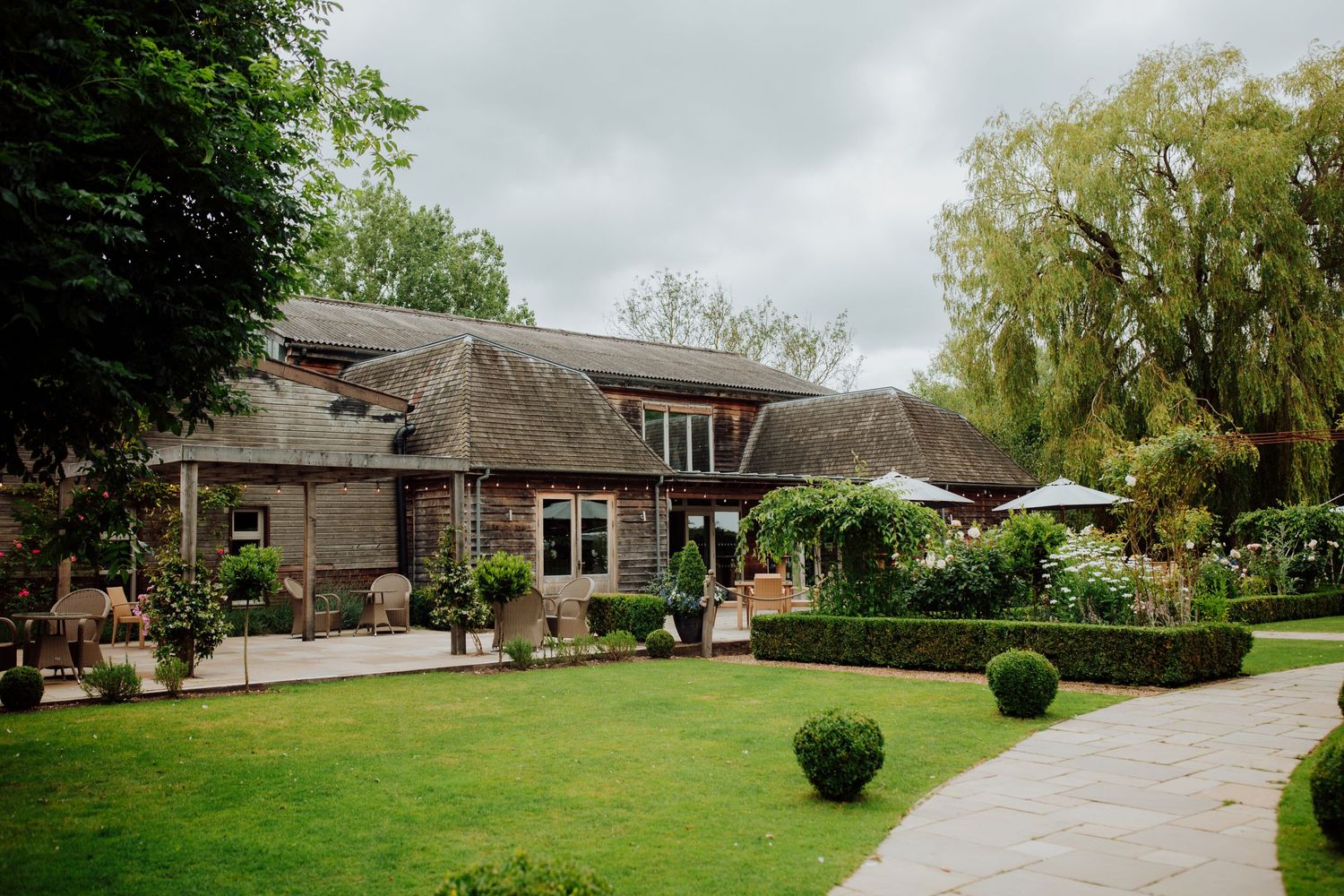Elegant country house venue with manicured lawn and curved driveway set against cloudy sky.