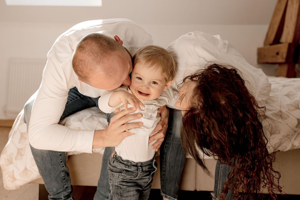 A family shares a joyful moment together on a white bed, creating a cozy and intimate atmosphere.