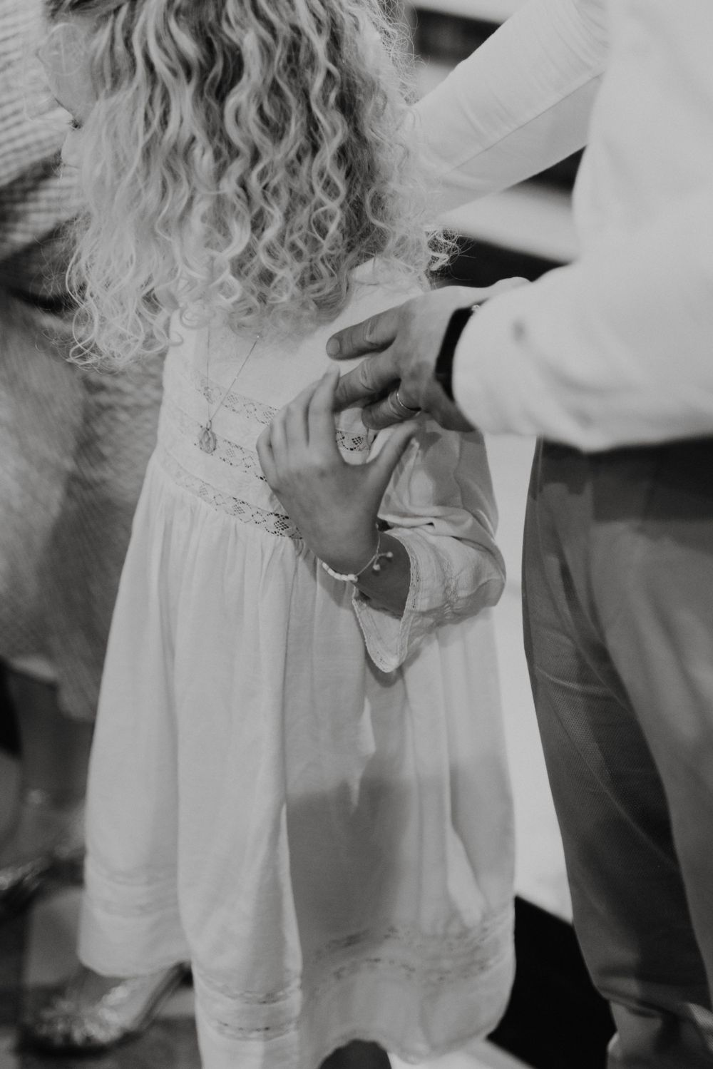 Photo en noir et blanc montrant le détail d'une robe en dentelle blanche et des mains.