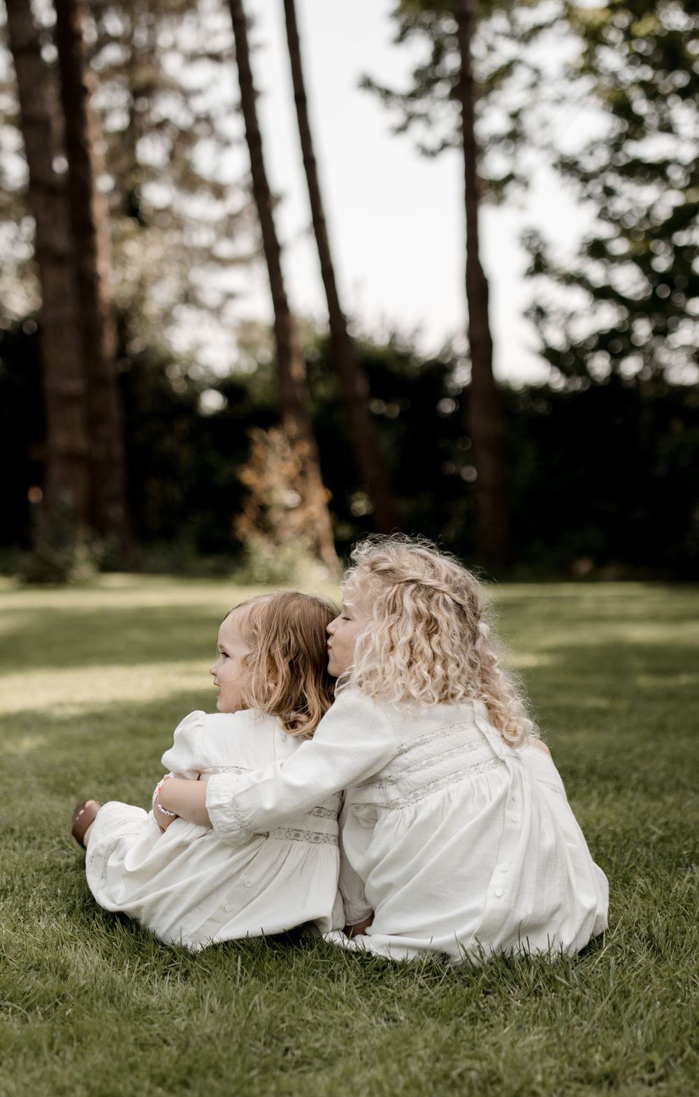Deux petites filles en robes blanches assises ensemble sur l'herbe avec des arbres en arrière-plan.