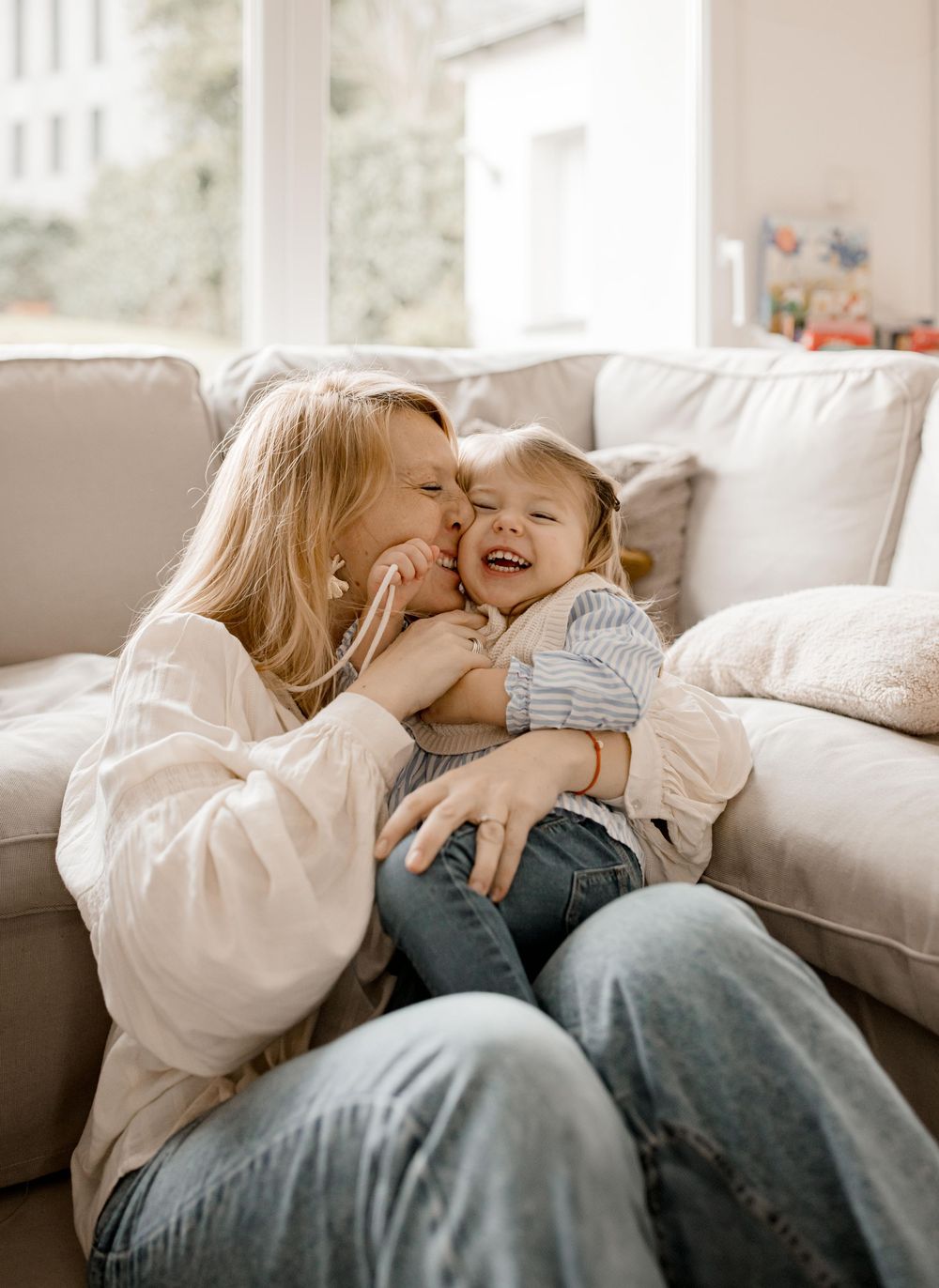 A tender moment of affection and laughter shared between parent and child on a cozy beige couch.