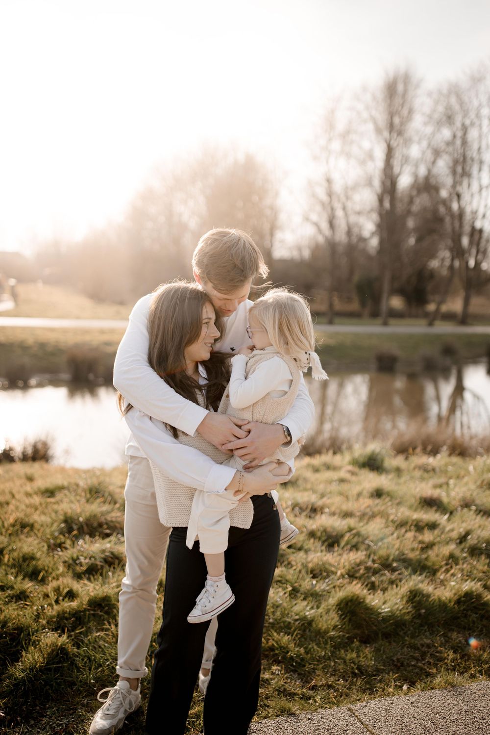 Family embraces together during sunset by a serene lake on a golden autumn evening in the park.