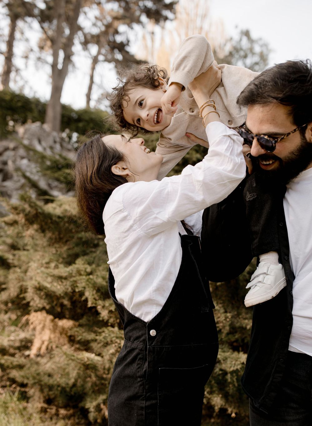 A joyful family moment outdoors with a small child being lifted up playfully against a natural woodland backdrop.