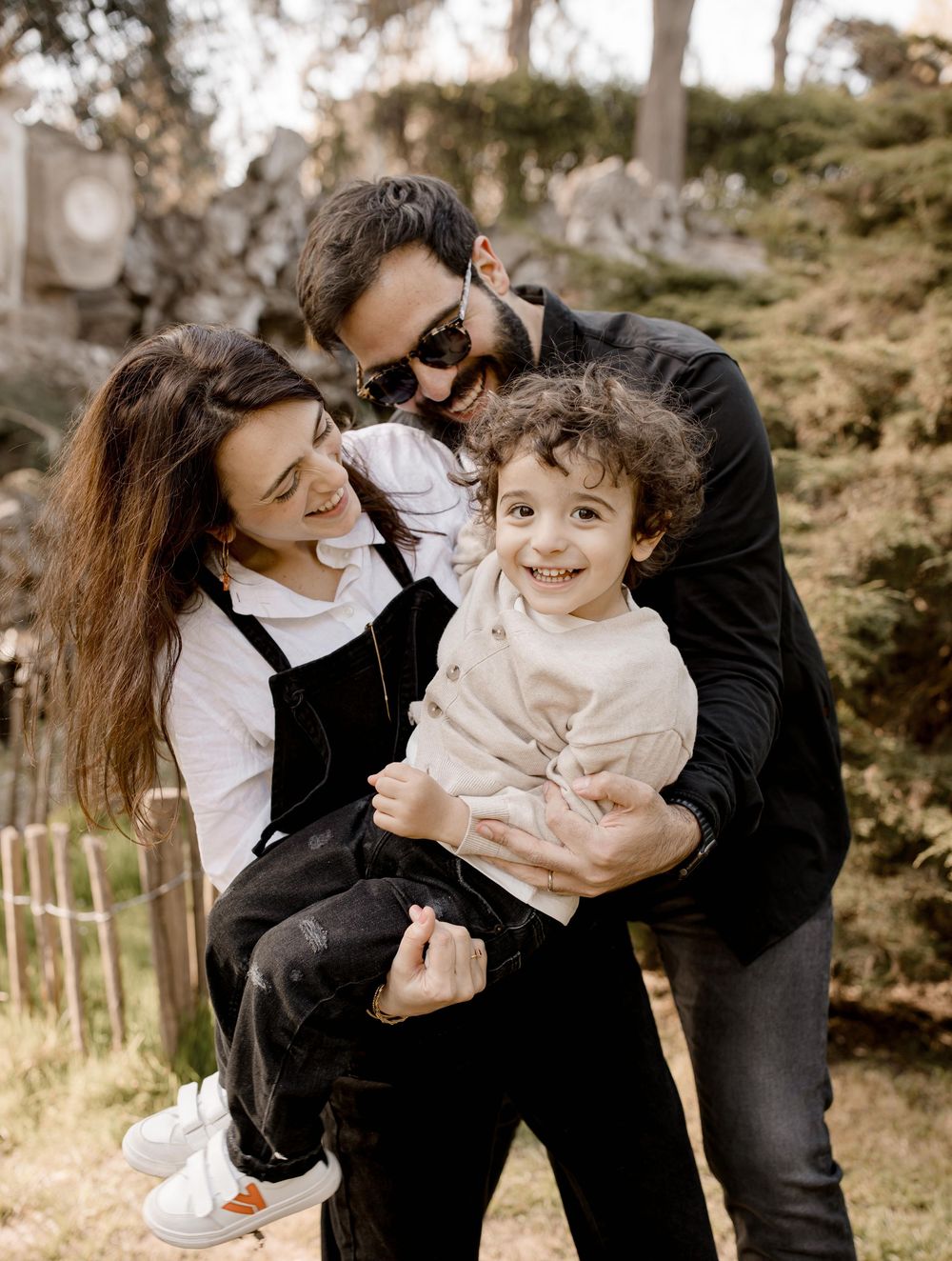 A loving family shares a tender moment together outdoors in a natural setting with sunlit trees in the background.
