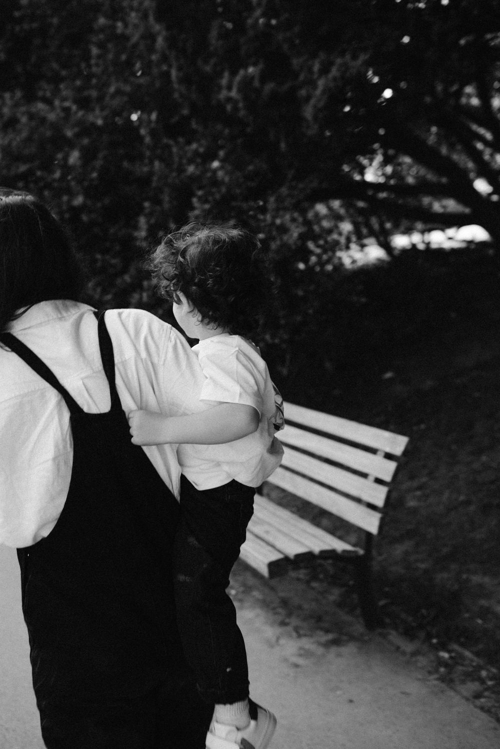 A black and white photo of an intimate moment between two people embracing near a park bench.