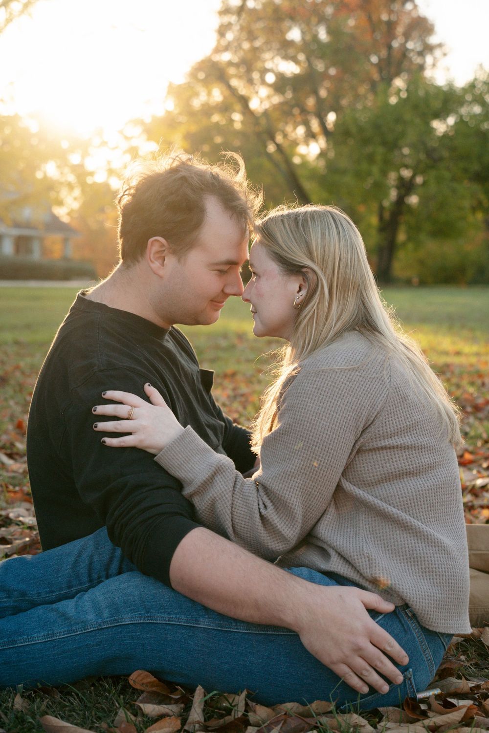 Couple sitting in fallen autumn leaves at golden sunset, embracing and touching foreheads romantically.