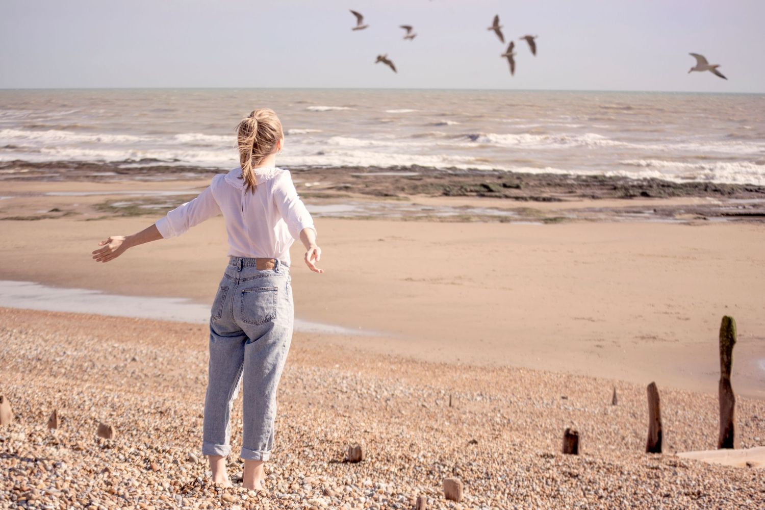 female arms wide facing see, wind blowing hair, seagulls flying in the sky