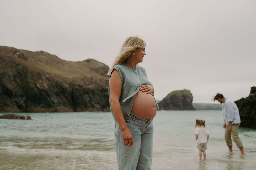 A maternity photo series captures intimate moments of a couple at a misty beach with mountains in the background.