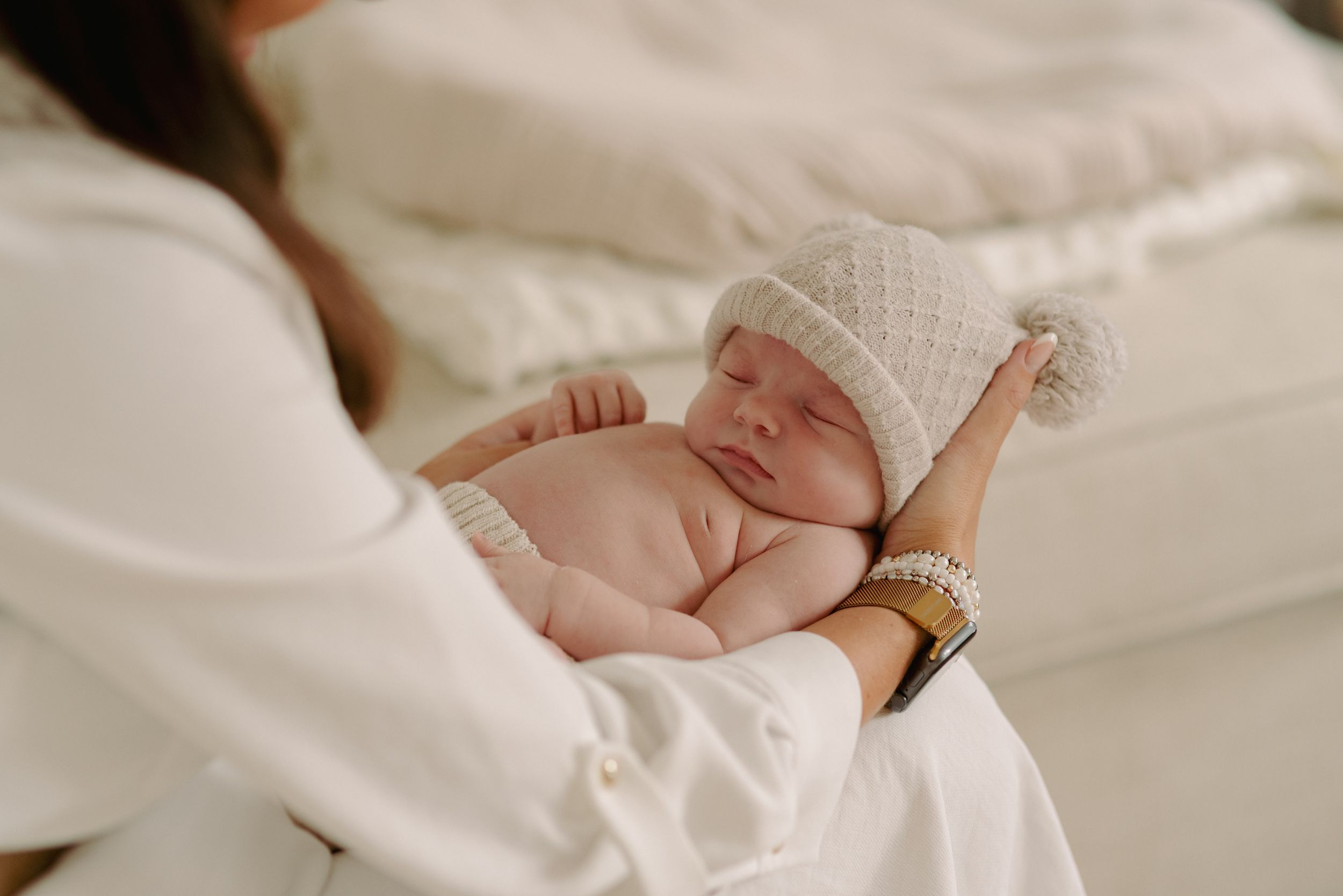 Peaceful sleeping newborn baby wearing soft white knit hat resting in white blankets.