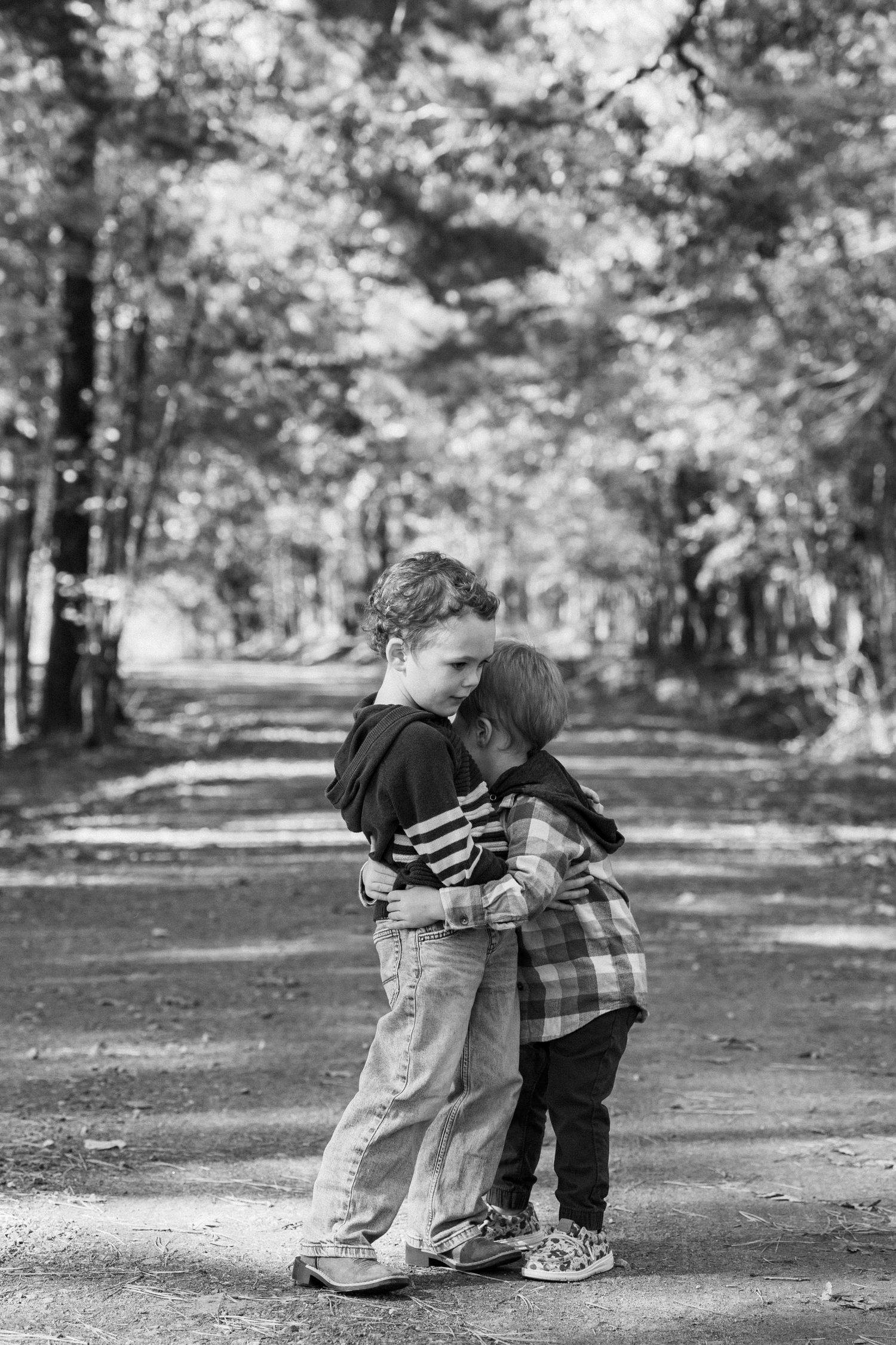 A black and white portrait of someone holding a small child outdoors near trees.