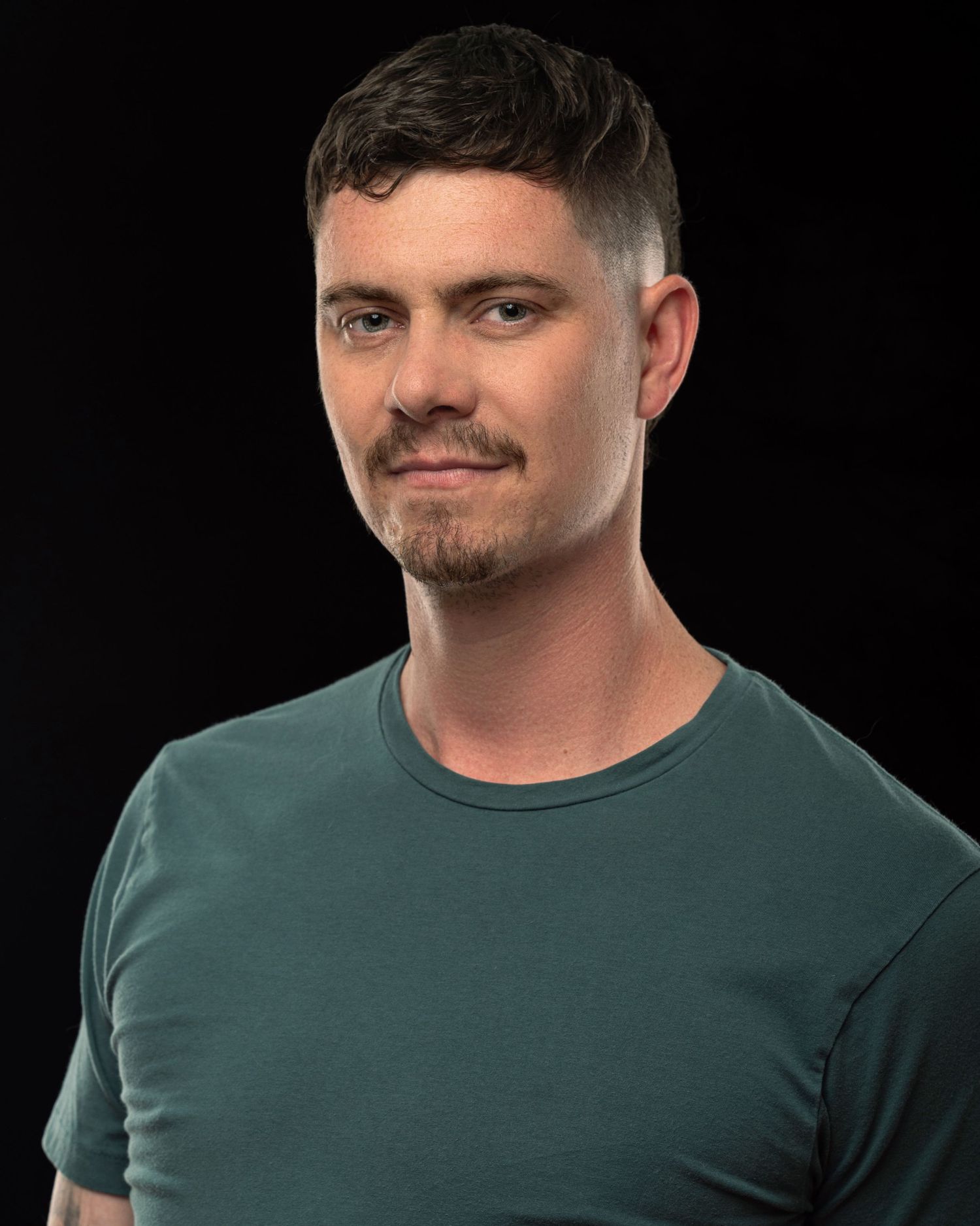 A professional headshot of a person in a green t-shirt against a black background.