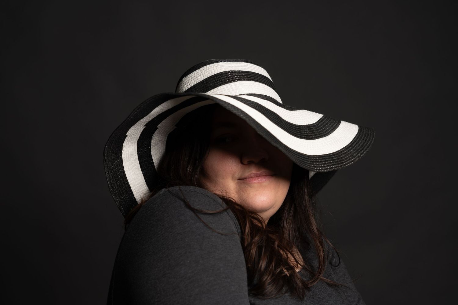 A striped black and white sun hat dramatic pose against dark background.