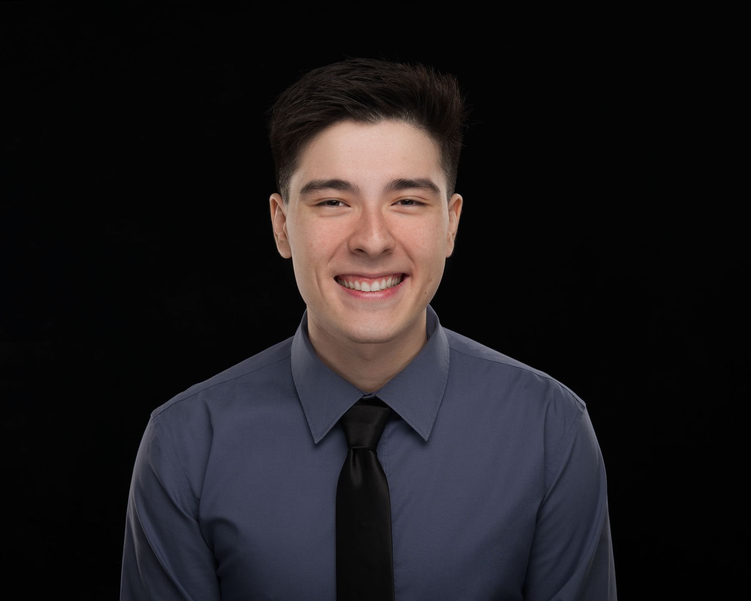 Professional headshot of someone wearing a navy dress shirt and black tie against a dark background.