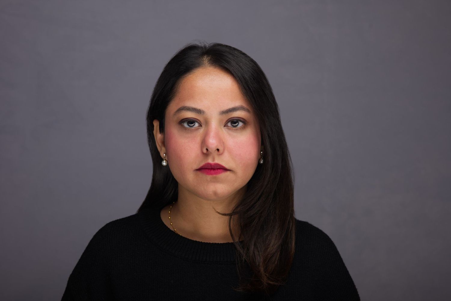 Professional portrait of a woman with long dark hair wearing a black top against a gray background.