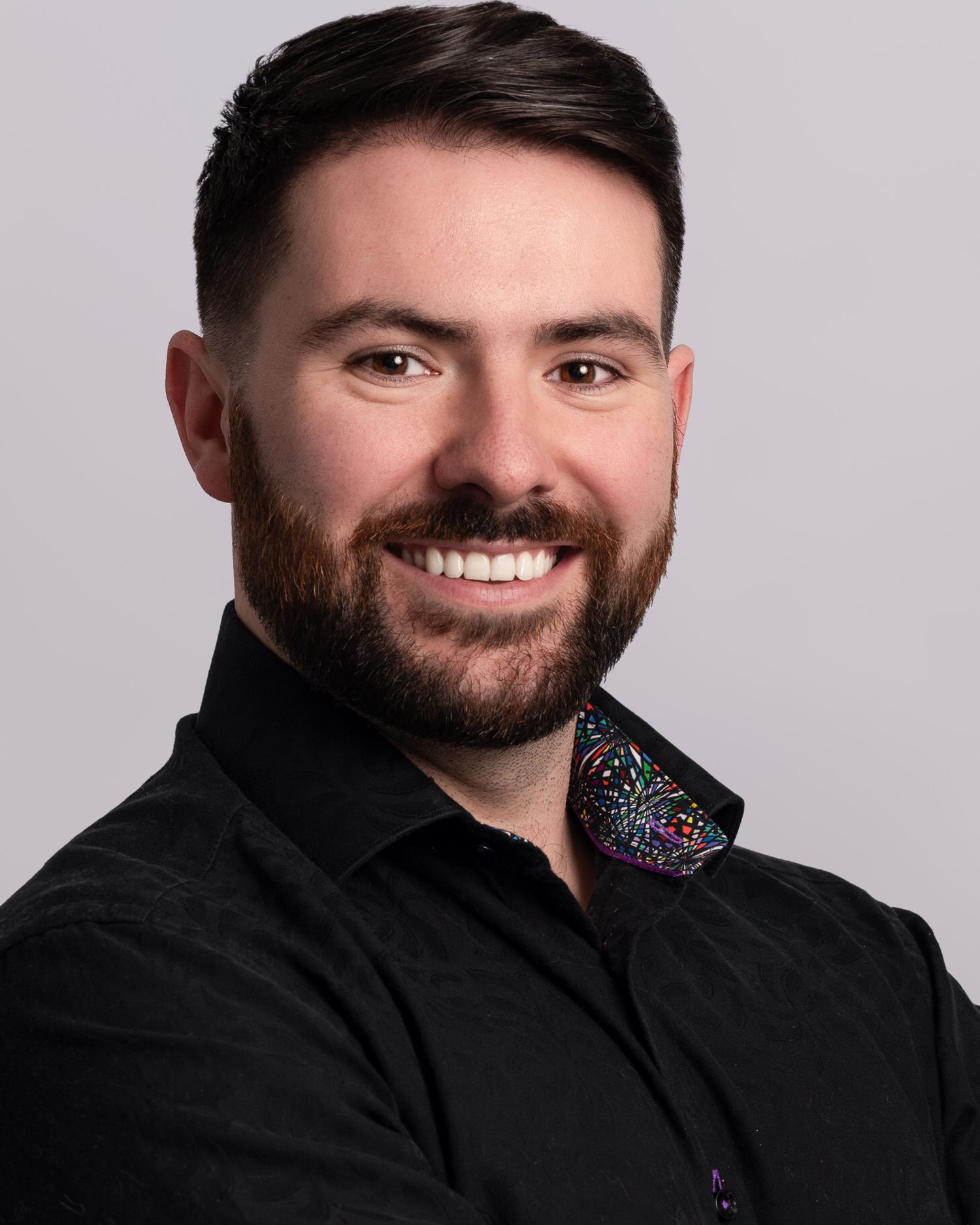 A professional headshot of a person in a black polo shirt against a gray background.