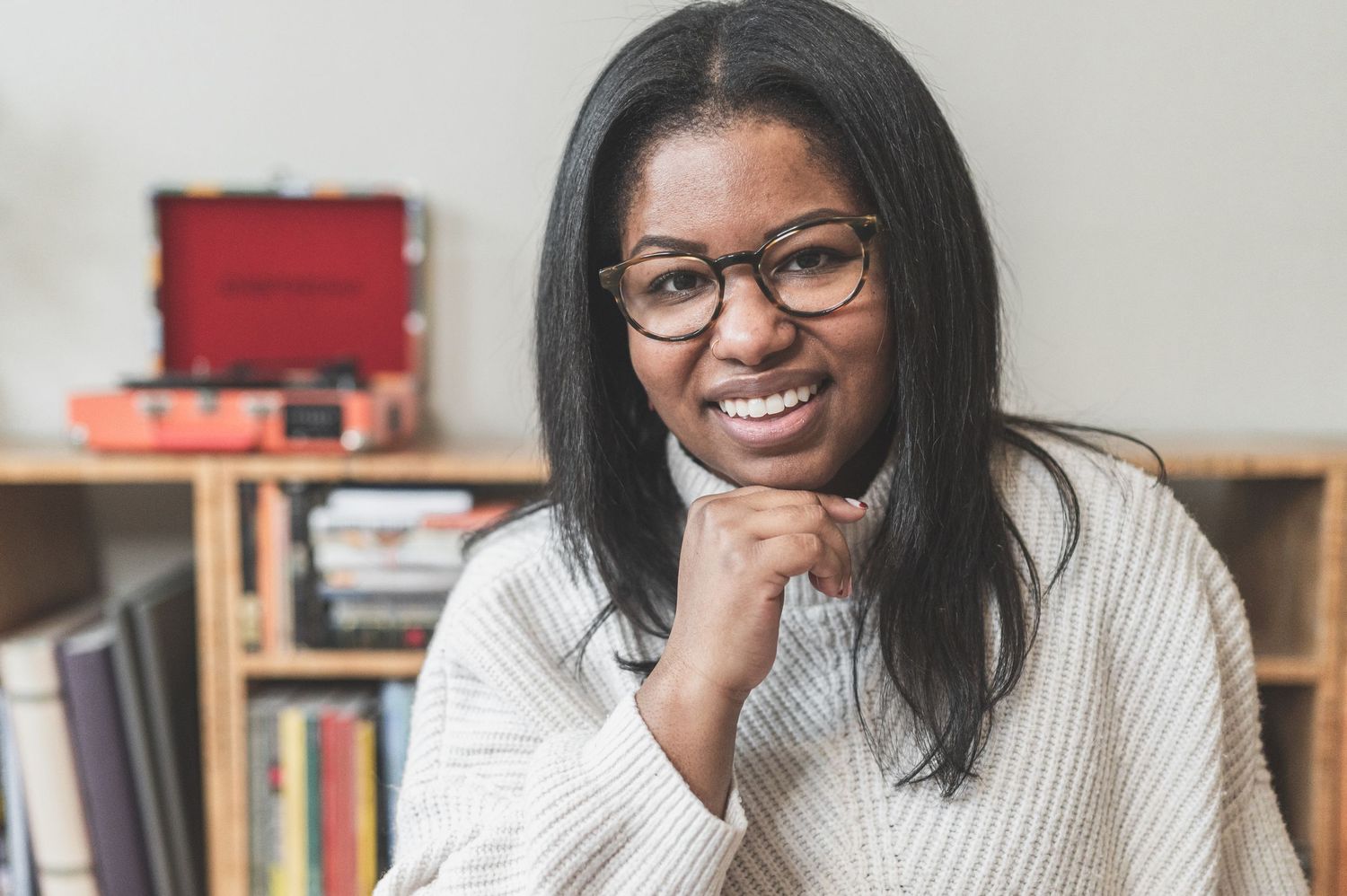 A casual portrait of a person in glasses and white sweater in front of a bookshelf.