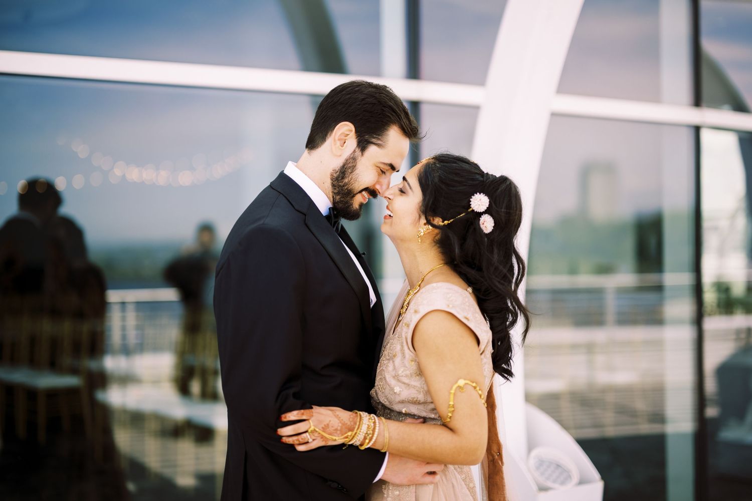 A loving couple shares an intimate moment on their wedding day in front of large glass windows.