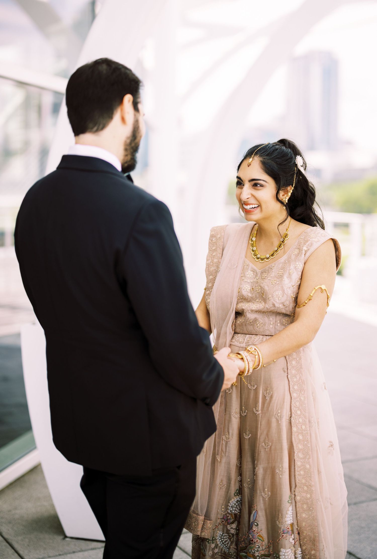 A couple in formal attire shares a joyful moment on their wedding day, with the bride wearing a blush pink embellished dress.