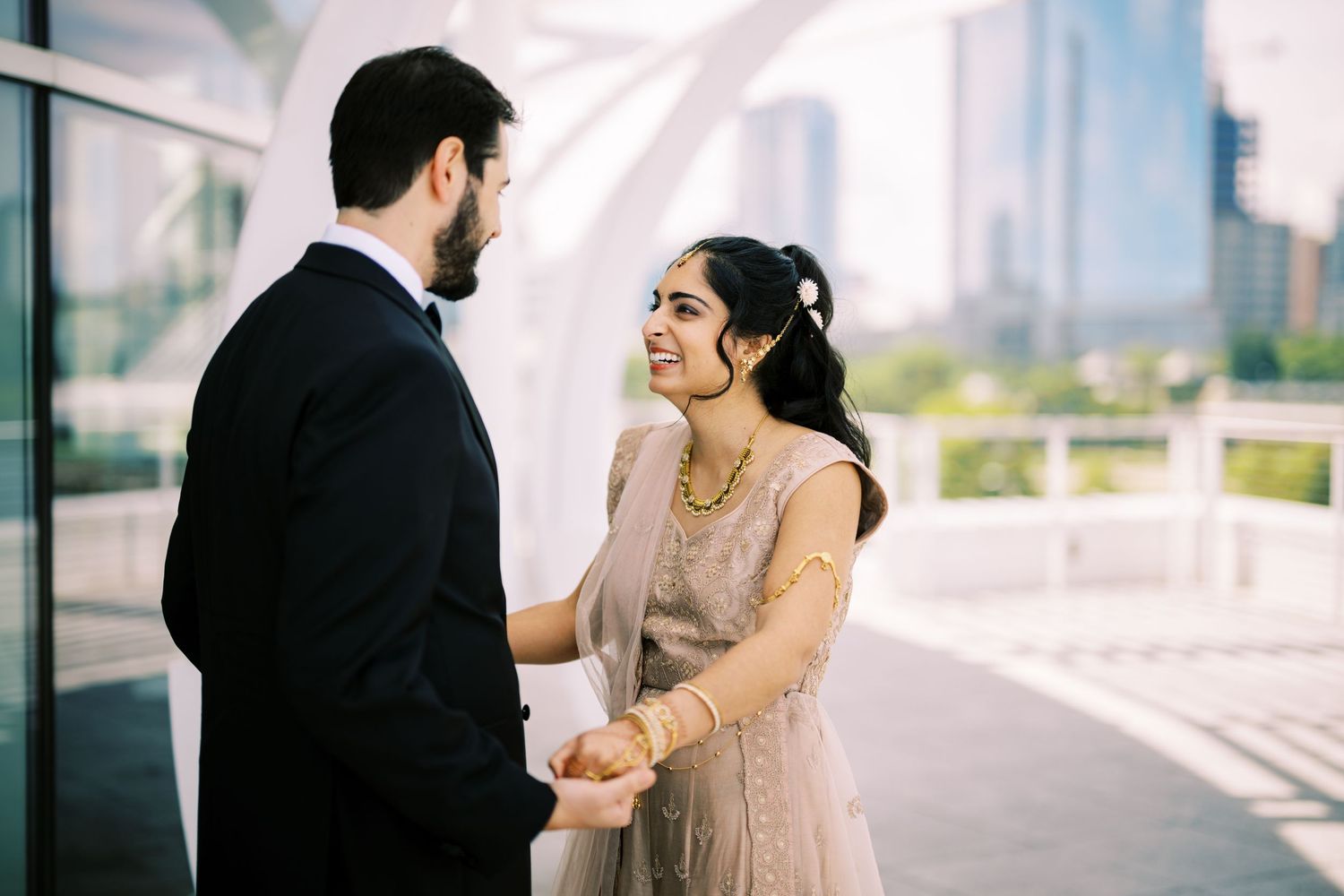 A couple shares an intimate moment outdoors, with the person in a beige gown smiling warmly at their companion.
