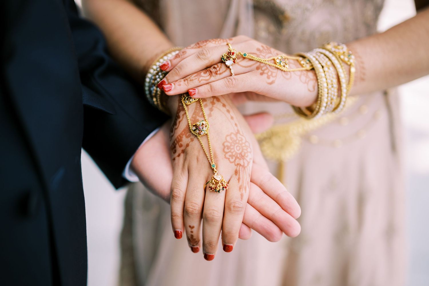 Hands adorned with traditional Indian bridal mehndi and gold bangles are held together during a wedding ceremony.