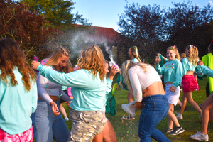 Students celebrating at an outdoor event with colorful powder and dancing.