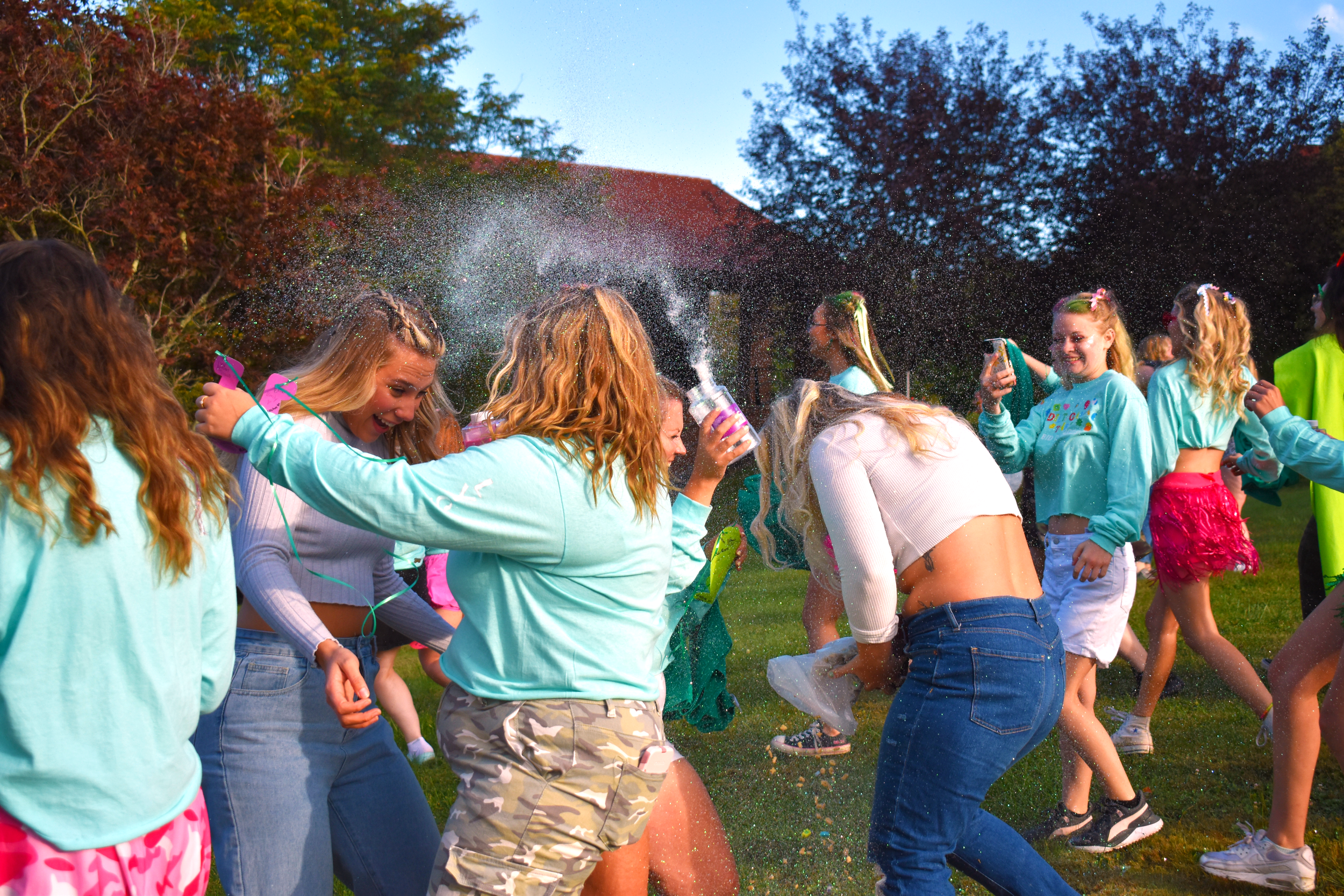 Students celebrating at an outdoor event with colorful powder and dancing.