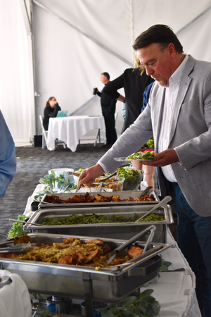 Someone in a gray suit serving themselves food from a buffet line with chafing dishes at a catered event.