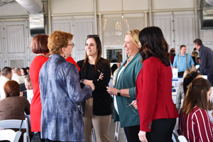 People networking and mingling during a professional event in a bright indoor venue with tables in the background.