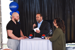 People engaged in discussion at a networking event with blue balloons and X-shaped decorations on a table.