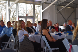 A group of people seated at tables during a gathering in a covered outdoor venue.
