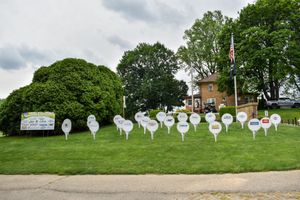 White cutout silhouettes of ghosts displayed on a grassy hillside by a church, creating a spooky Halloween display.