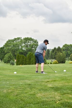 A golfer in blue shorts and gray shirt lines up to practice putting on a lush green golf course fairway.