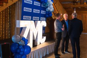 Three men networking at a ZMC Chamber event with blue and white balloon decorations and illuminated letter display.