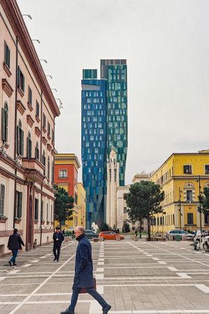 Modern blue glass skyscraper contrasts with traditional buildings on a paved street. Tirana, Albania,